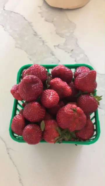 A green basket filled with strawberries on top of a table.